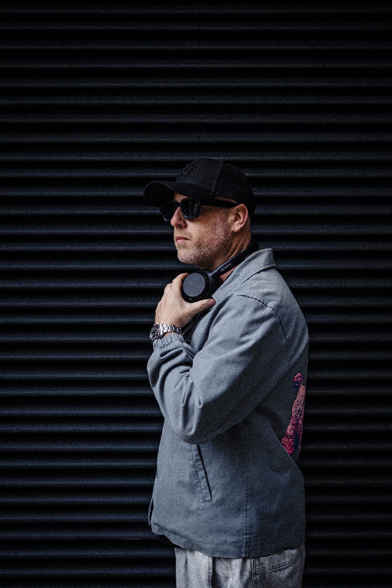 Biblical Beats in profile against a dark shutter, headphones in hand